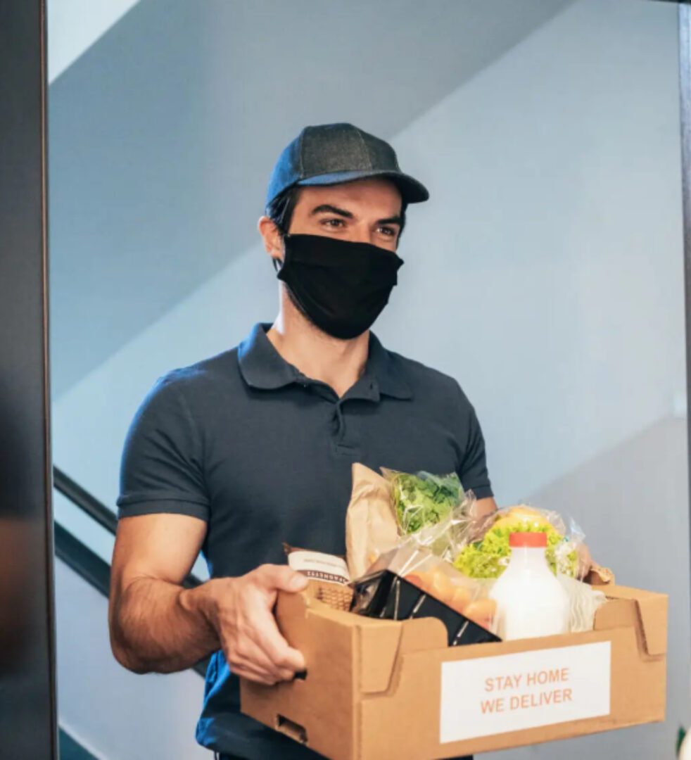 A man holding a box of food wearing a black mask.