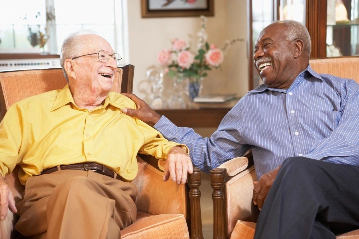 Two older men sitting in a chair laughing.