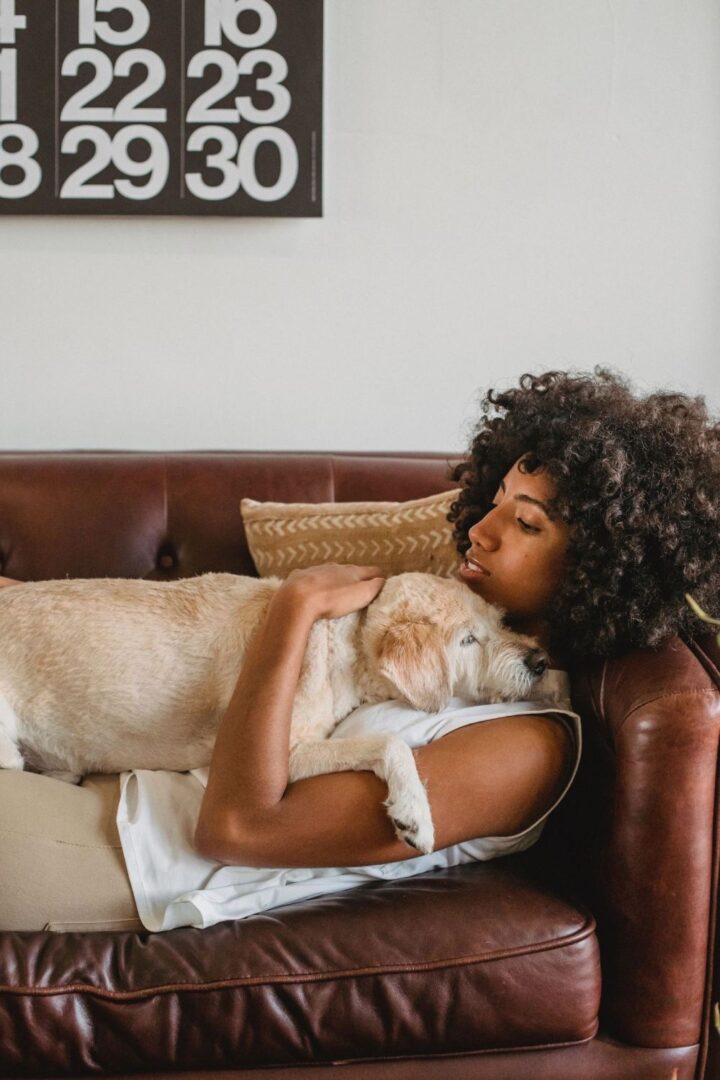 A woman is laying on the couch with her dog