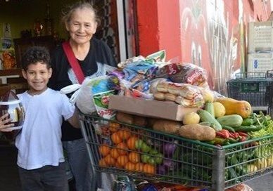 A woman and boy standing next to a shopping cart filled with fruit.